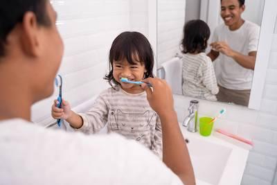 father teaching his daughter how to brush her teeth